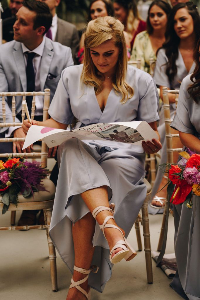 A guest enjoys singing songs from a personalised ceremony song sheet during an Autumn wedding