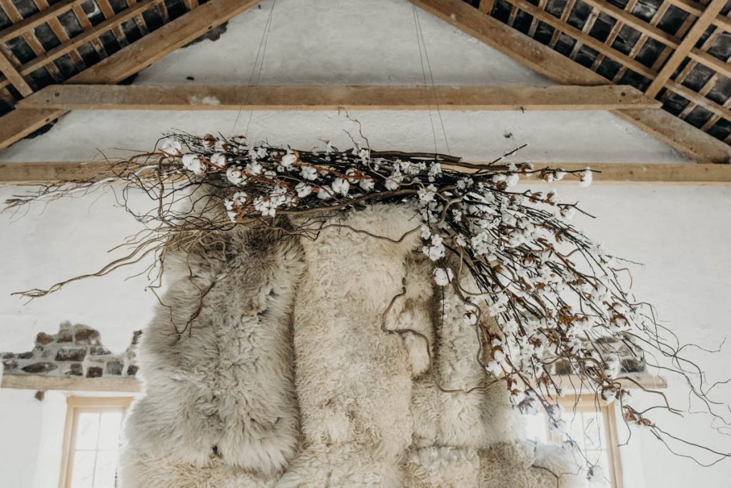 A sheepskin wedding ceremony backdrop styled with twigs, cotton and blossom for a modern barn wedding
