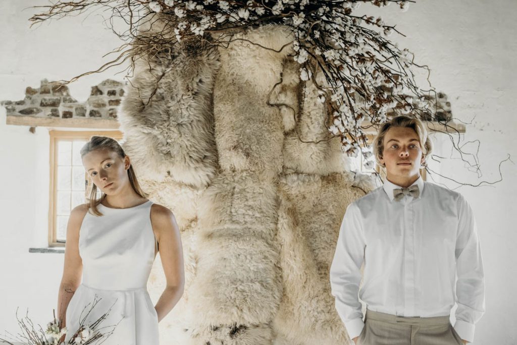 A sheepskin wedding ceremony backdrop styled with twigs, cotton and blossom for a modern barn wedding
