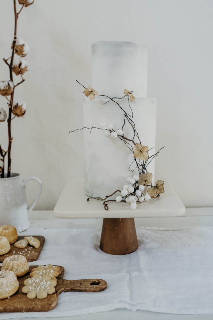 A beautiful two tier wedding cake on a wooden stand, decorated with twigs and cotton