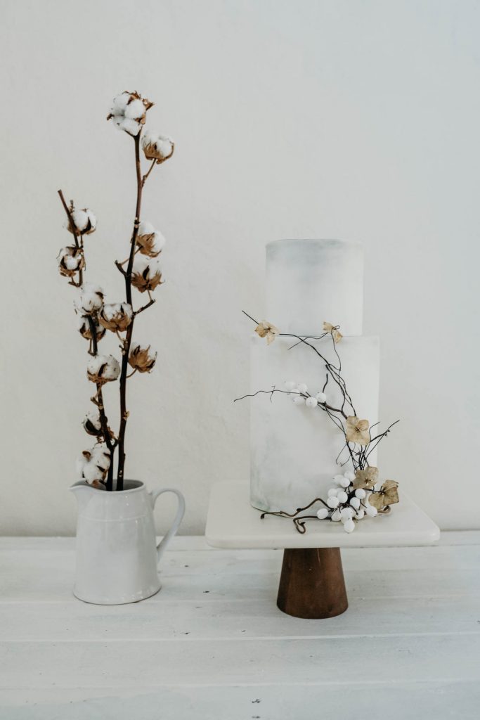 A contemporary 2 tier wedding cake decorated with simple twigs for a modern barn wedding