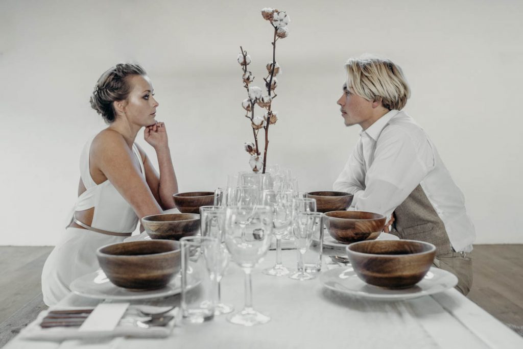 A bride and groom dine at a clean, modern wedding breakfast tablescape of neutral tones and wooden accents