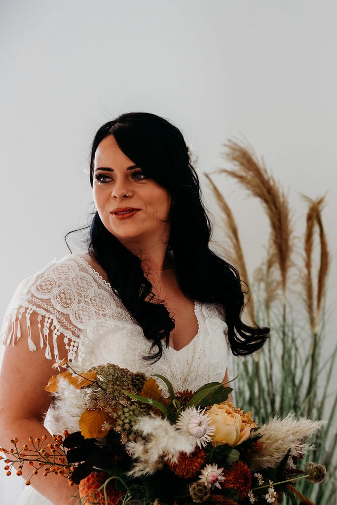 Bride wearing a bespoke Maggie Sottero boho style wedding dress with tasselled sleeves and a detachable veil cape