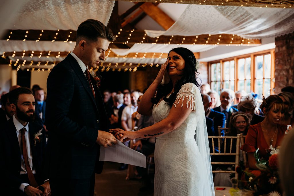 A bride in a boho style wedding dress wipes a tear from her eye during an emotional wedding ceremony