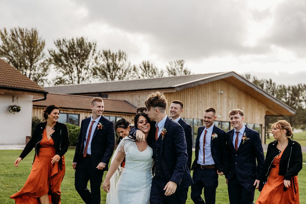 A groom gives his new wife a tender kiss on the forehea as they head outside for photos with their bridal party on their Autumn wedding day