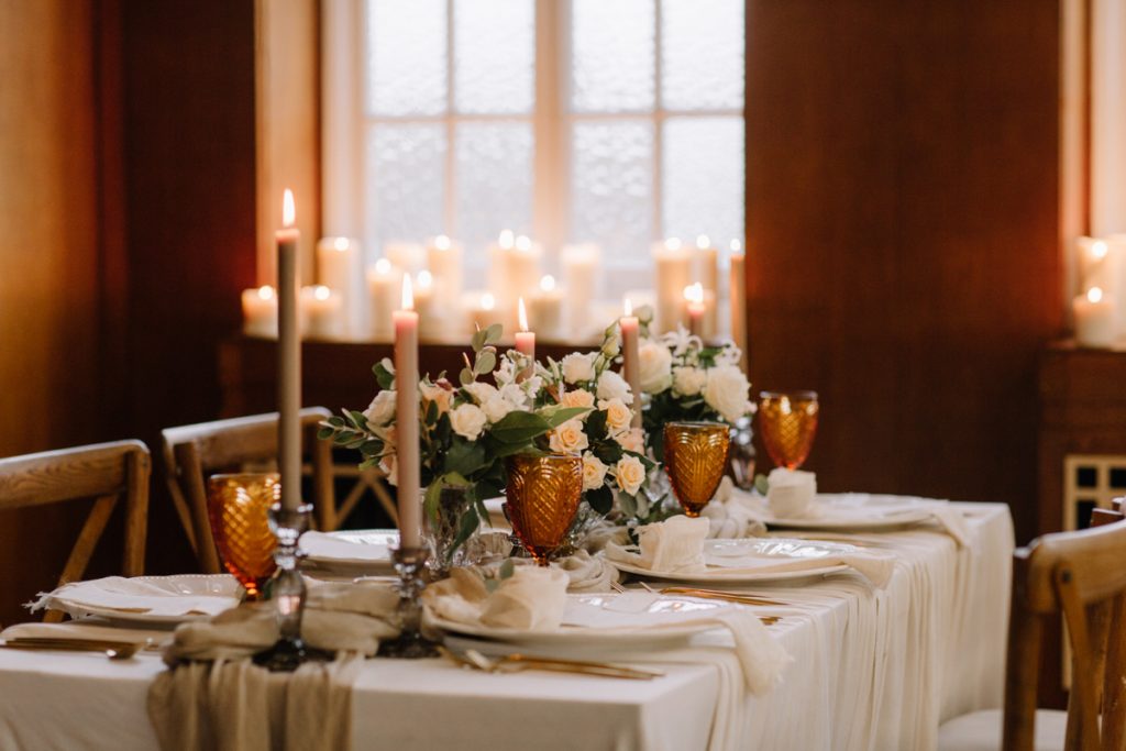 A winter wedding table with cream linen textured cloths and a colour palette of ambers, greens and a hint of gold