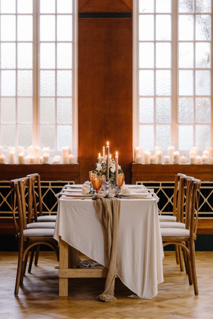 A winter wedding table with cream linen textured cloths and a colour palette of ambers, greens and a hint of gold