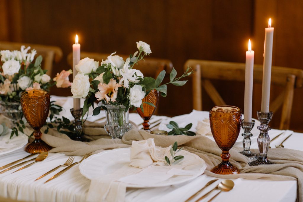 A winter wedding table with cream linen textured cloths and a colour palette of ambers, greens and a hint of gold