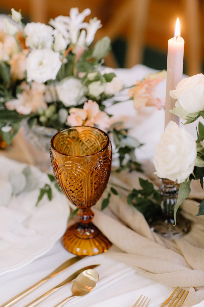 A winter wedding table with cream linen textured cloths and a colour palette of ambers, greens and a hint of gold
