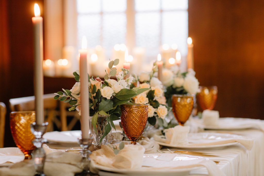 A winter wedding table with cream linen textured cloths and a colour palette of ambers, greens and a hint of gold