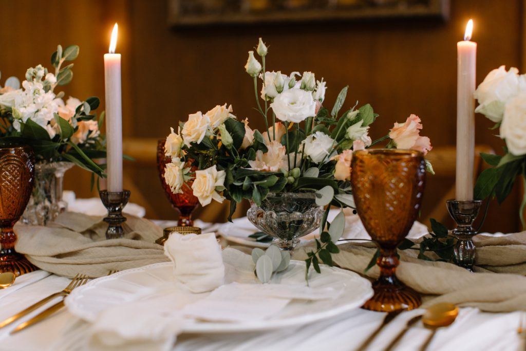 A winter wedding table with cream linen textured cloths and a colour palette of ambers, greens and a hint of gold