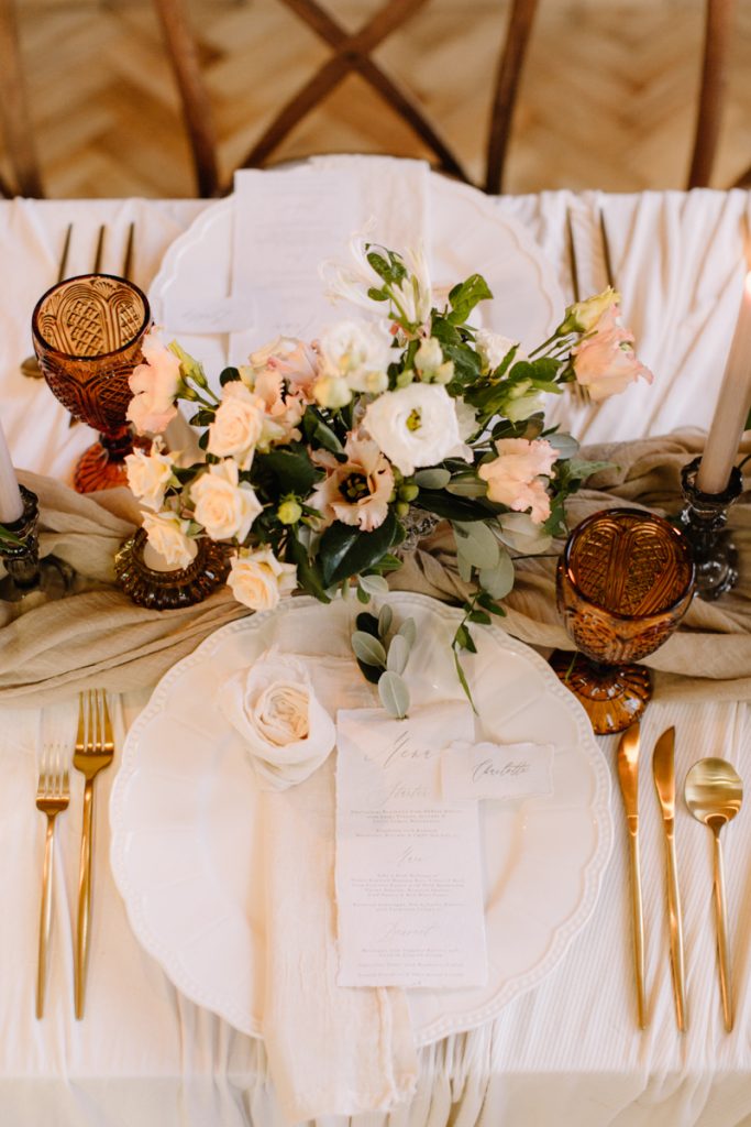 A winter wedding table with cream linen textured cloths and a colour palette of ambers, greens and a hint of gold