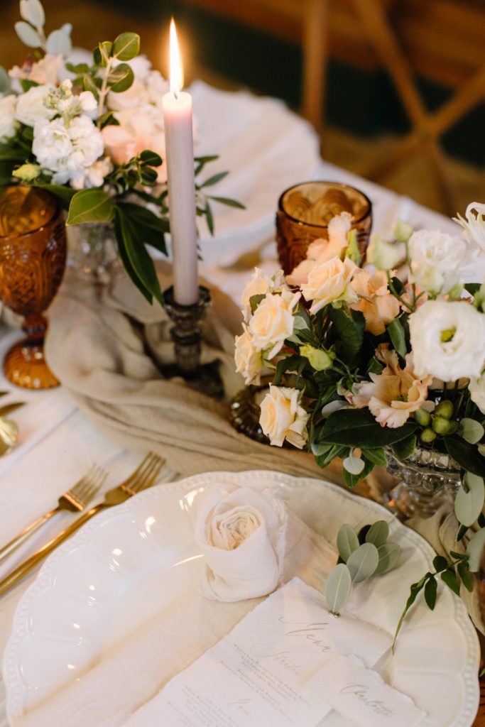 A winter wedding table with cream linen textured cloths and a colour palette of ambers, greens and a hint of gold