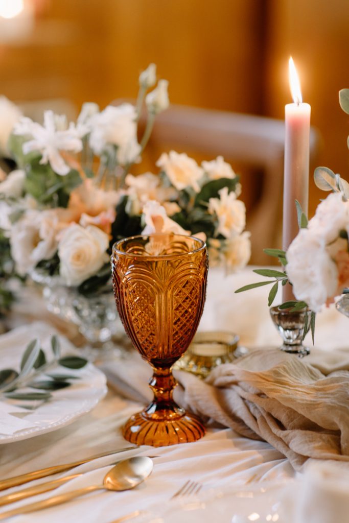 A winter wedding table with cream linen textured cloths and a colour palette of ambers, greens and a hint of gold