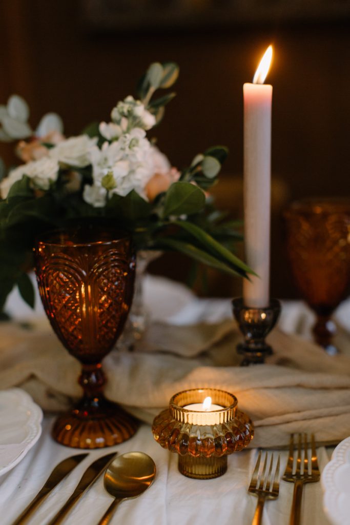 A winter wedding table with cream linen textured cloths and a colour palette of ambers, greens and a hint of gold