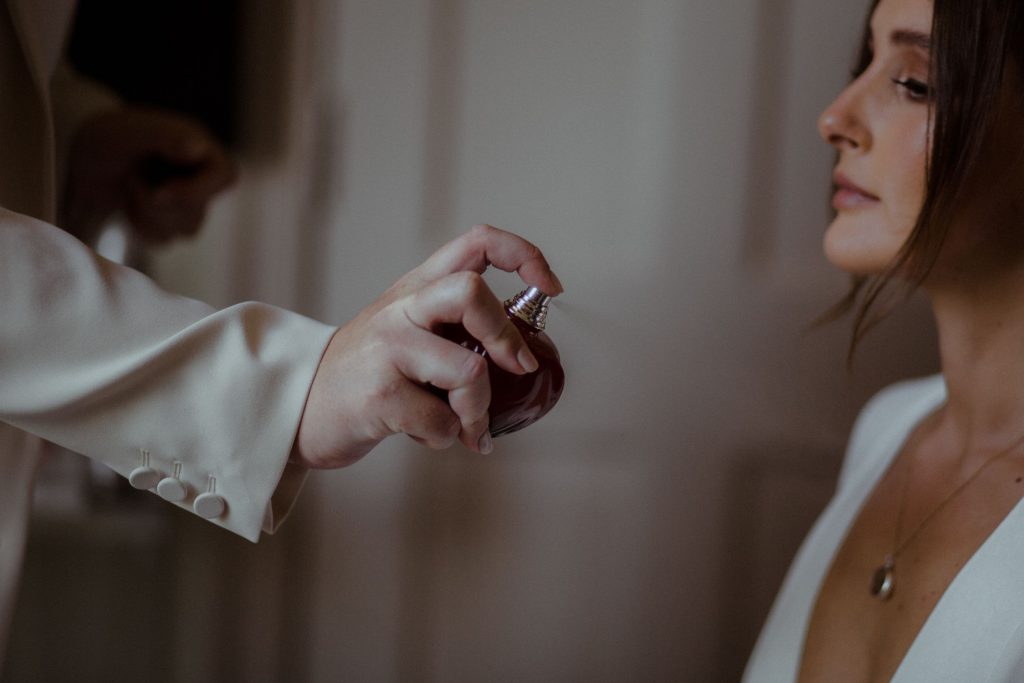 A bride is being sprayed gently with perfume by her best friend on the morning of her wedding