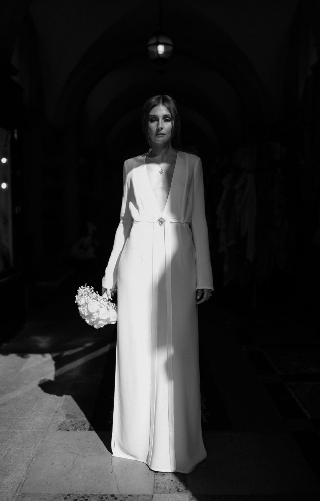 Bride Katja wearing a long sleeved Galvan London dress bathed in sunlight whilst holding a small elegant wedding bouqiet