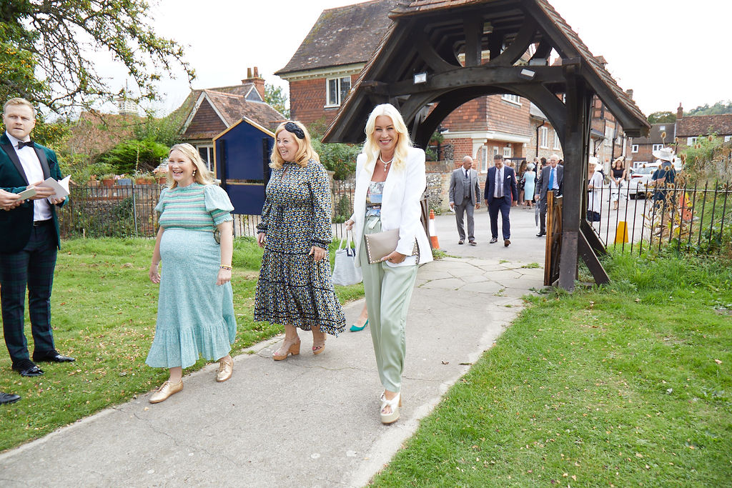 Guests arrive at a Church prior to a wedding taking place. The guests are dressed in glamourous outfits and are all smiling and happy