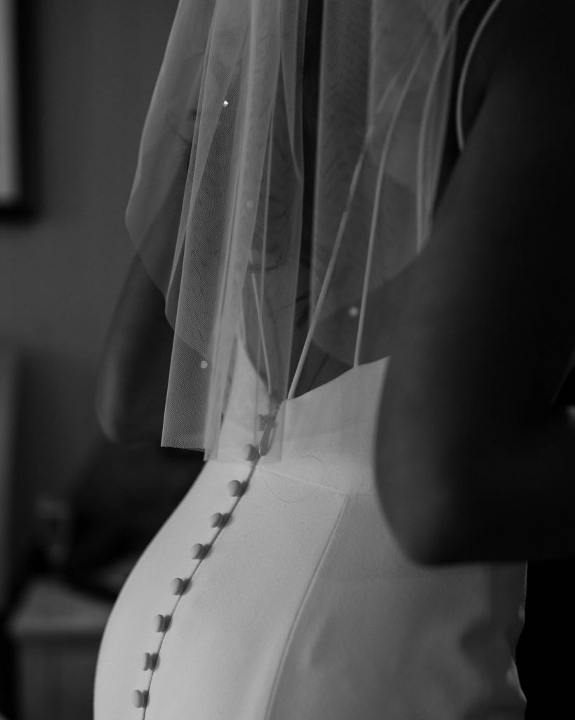 A beautifully detailed close up black and white image of a wedding dress back with button details and a short sheer wedding veil