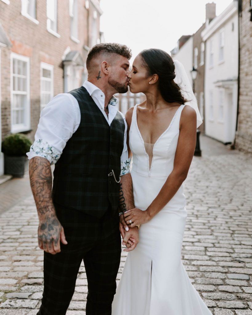A bride and groom hold hands and kiss gently in the quiet streets during their couple shots on their wedding day