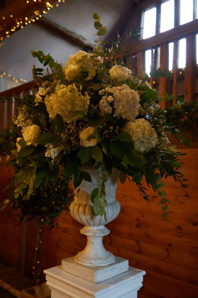 A large green and white classic floral display on top of a plinth to decorate the wedding breakfast space at Lains Barn for a classic wedding