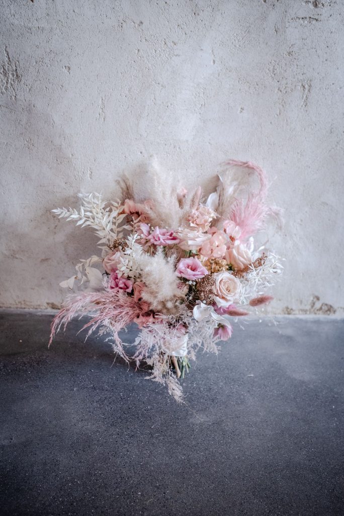 A pale pink and cream wedding bouquet of fresh and dried flowers with soft pampas grass is displayed on the floor for a pastel boho wedding shoot.