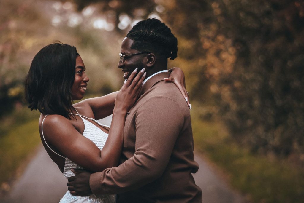 A newly wed couple enjoy an intimate wedding photo shoot in a forest. They look at each other with wides smiles as she caresses his face with her right hand and he holds her gently around the waist.