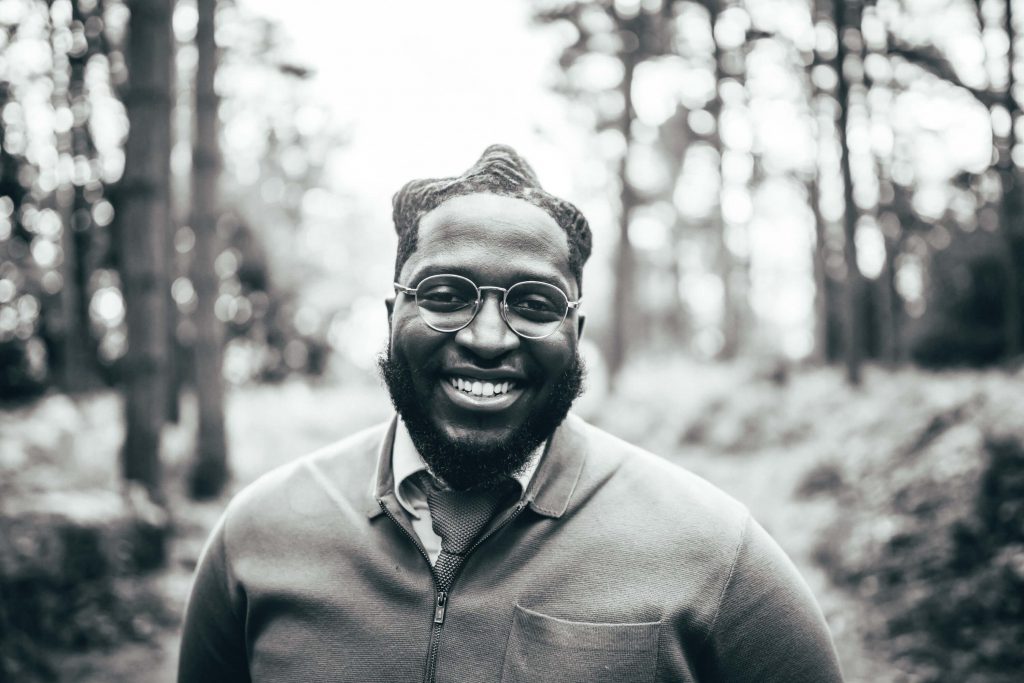 A groom smiles broadly as he looks directly into the camera in a black and white portrait shot. He grins as he celebrates his wedding day in an intimate wedding photo shoot.