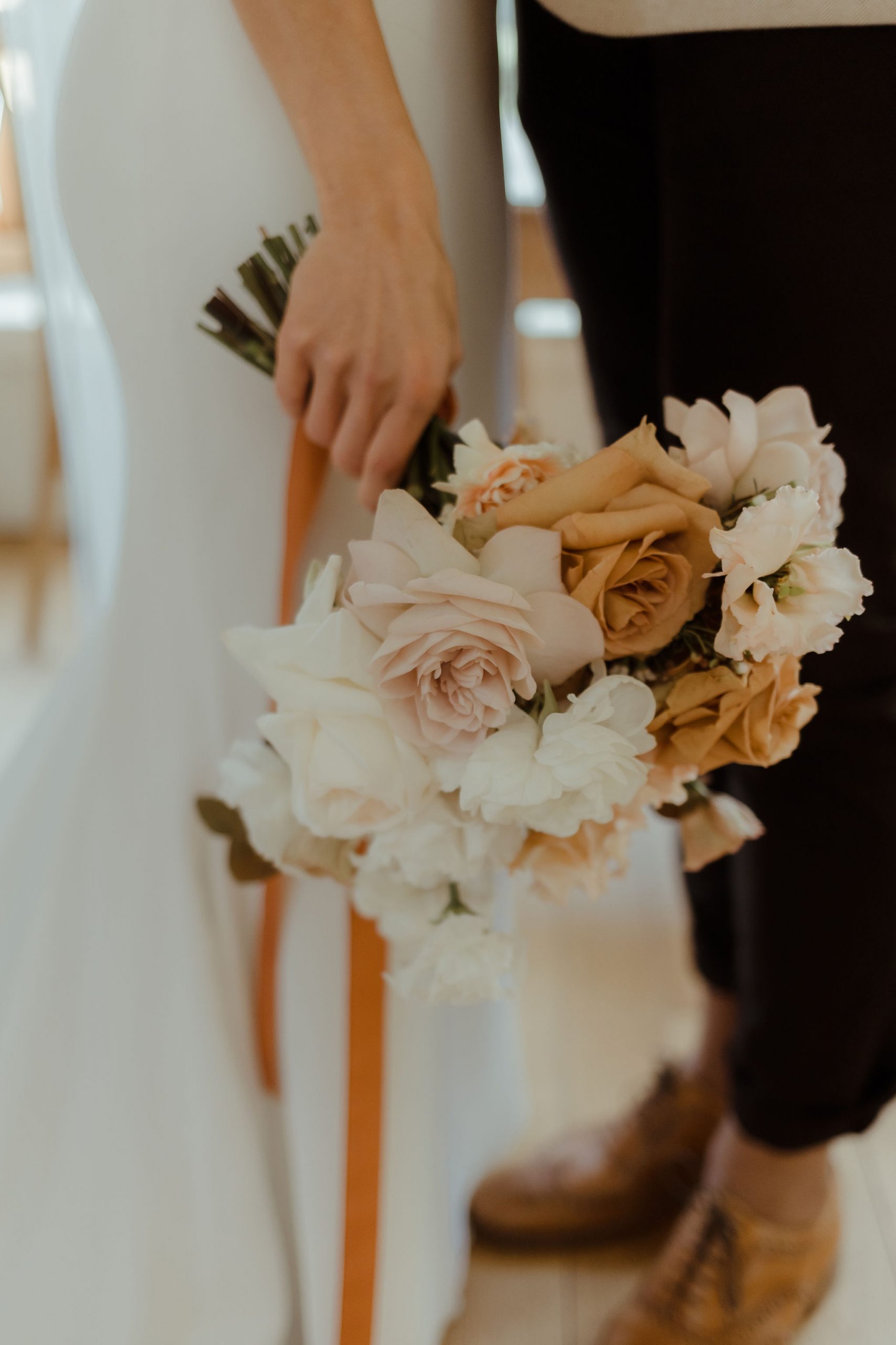 A hand holds a beautiful wedding bouquet of toffee and cream roses.