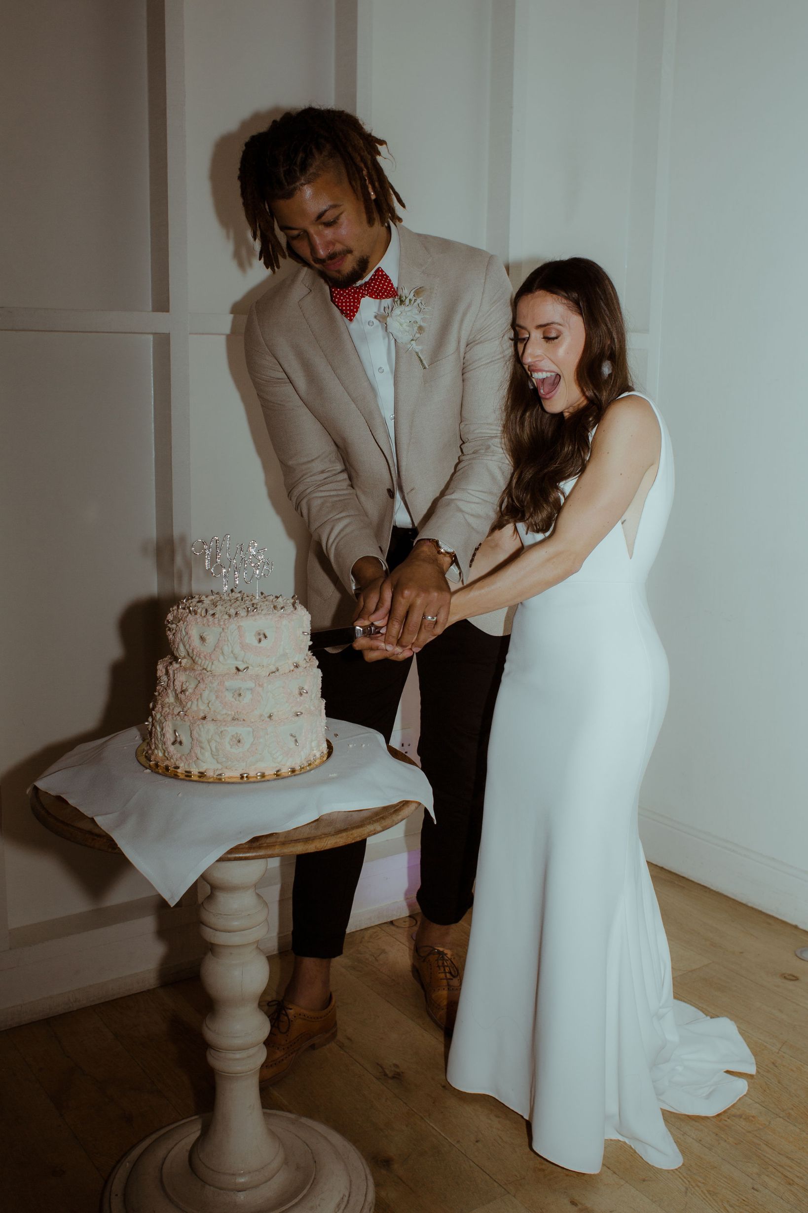 There is a bride and groom cutting their wedding cake. The bride laughs joyfully.