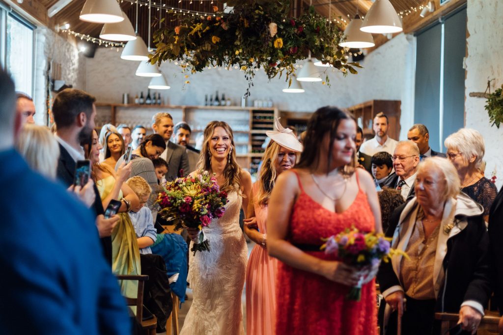 Bride Louise walks up the aisle, arm in arm with her Mum