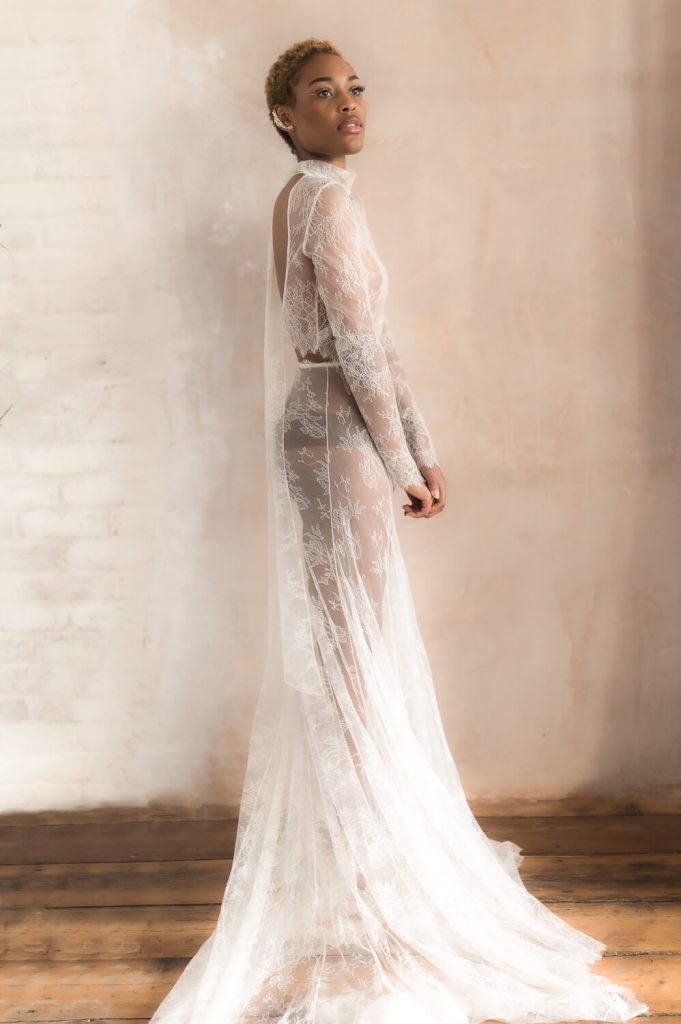 A sexy modern bridal look of a delicate French lace contemporary wedding dress with a daring cut out back and long sleeves. The dress is very sheer, exposing the woman's body underneath it. She wears dark brown underwear.