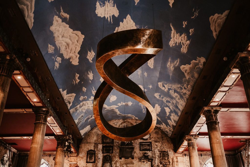 A contemporary ceiling installation at Bristol's wedding venue The Mount Without. The huge modern figure of 8 style installation hangs from the ceiling, modern looking in contrast to the distressed, crumbling walls of the historic Grade II listed building.
