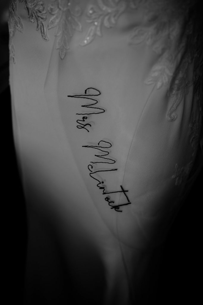 A black and white close up image of a contemporary wedding veil. Black hand sewn script thread spells our Mrs McLintock, the bride's new surname, on the veil.