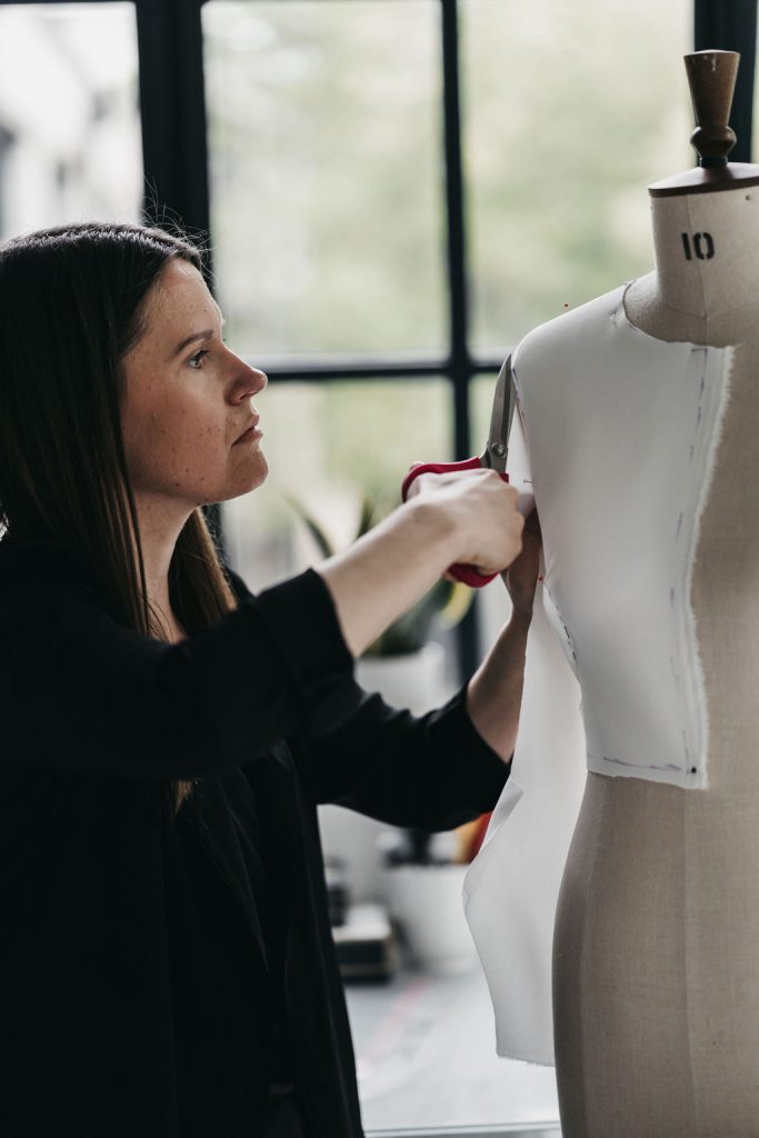 A bridal designer cuts through cotton toile on a mannequin as she makes the mock up of a wedding dress at its initial stage.