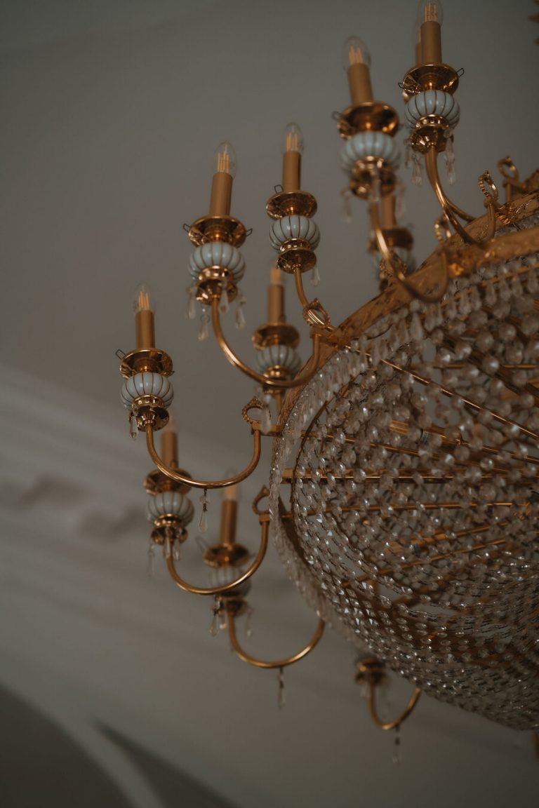 An opulent, elegant yet modern chandelier hangs from a ceiling boasting gold detailing.