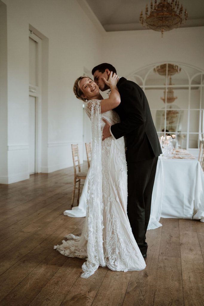 An elegant wedding dress features delicate, intricate hand beaded lace and a dramatic detailed cape.