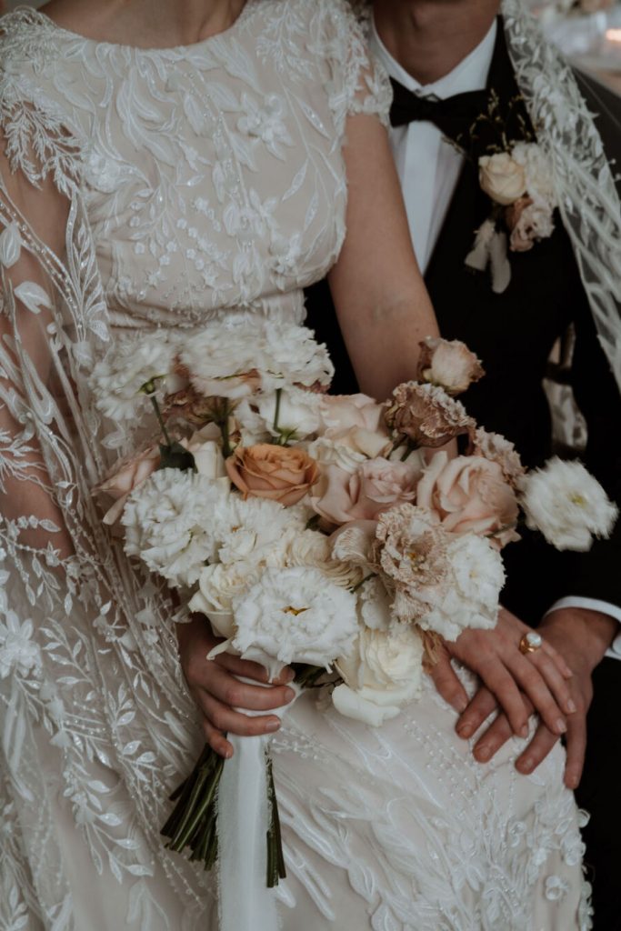 An elegant wedding dress features delicate, intricate hand beaded lace and a dramatic detailed cape.