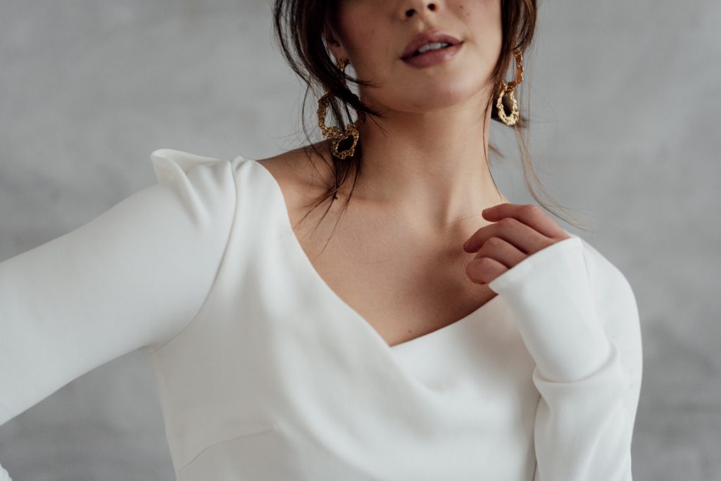 A bride wears a minimalist white wedding dress with long sleeves made with ethical and sustainable, vegan fabrics.