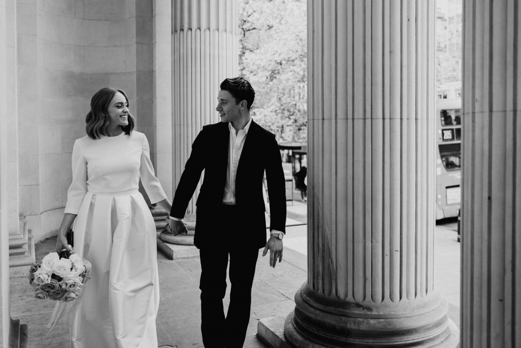A newlywed couple have couple portraits taken just after their wedding ceremony at London's iconic Old Marylebone Town Hall. The large Corinthian columns can be seen in the background and the famous white stone walls of the building.