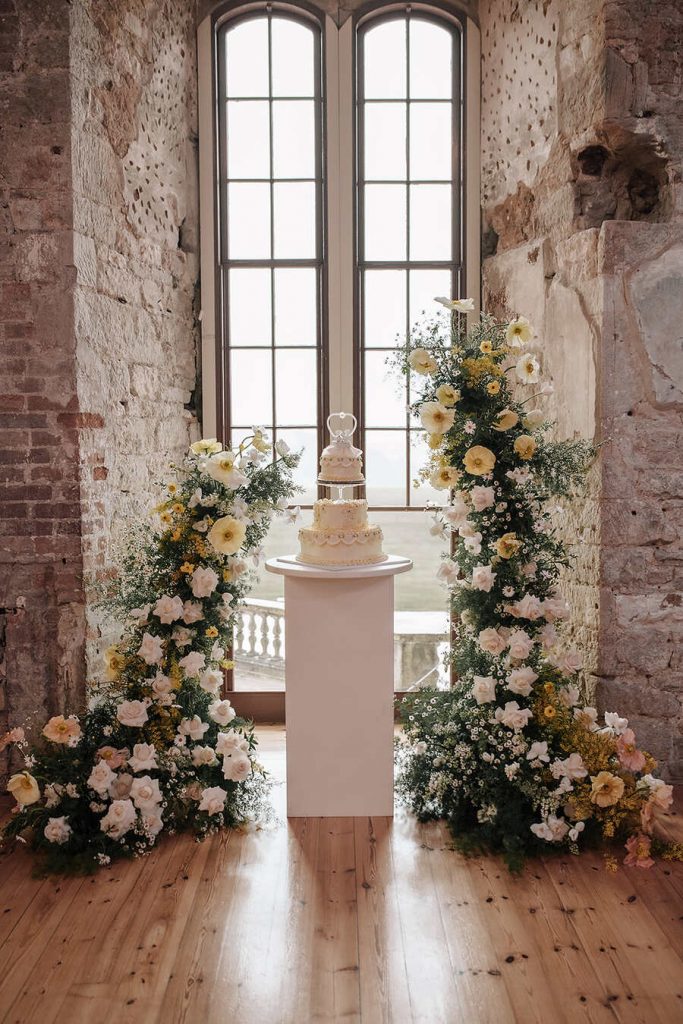 A soft yellow heart shaped vintage style cake framed with deconstructed floral arches