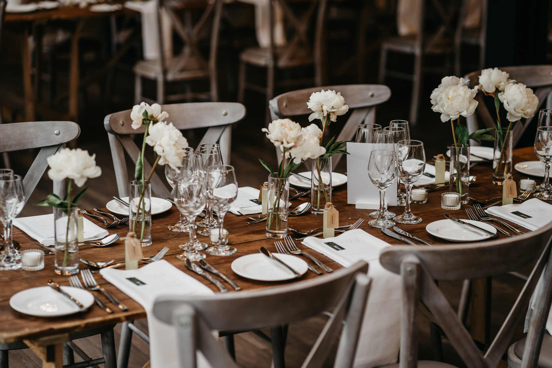 Minimalist table styling with hundreds of individual stems of white peonies lining the wooden tables