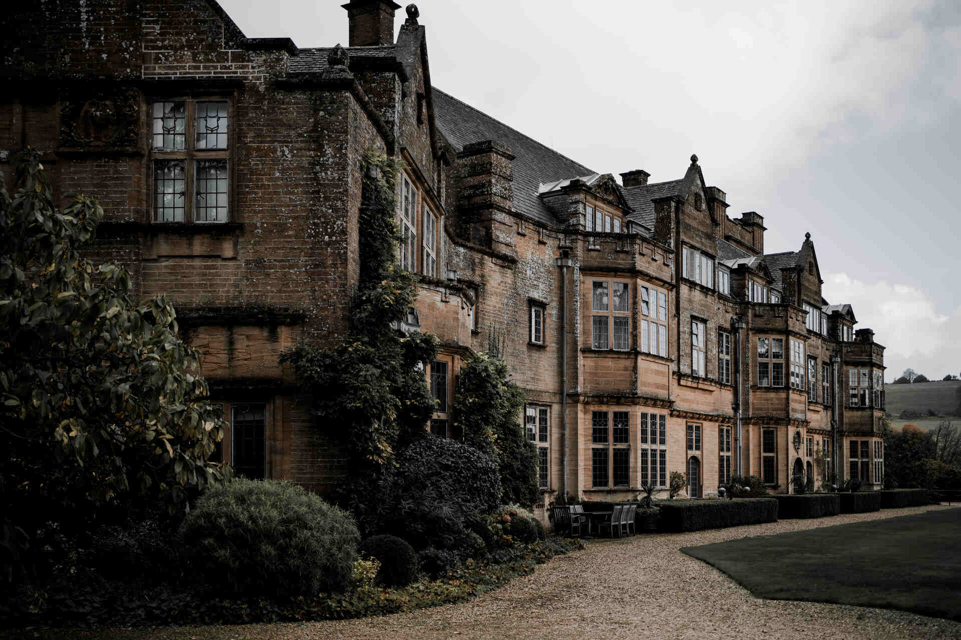 An imposing, stately, grand country manor house surrounded by lush greenery and manicured gardens.